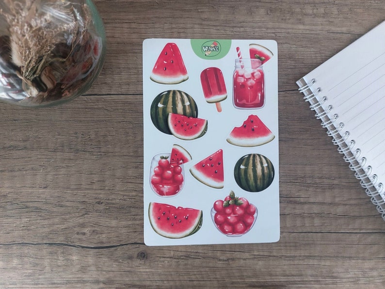 May include: A sheet of stickers featuring watermelon illustrations. The stickers include watermelon slices, watermelon wedges, whole watermelons, a glass of watermelon juice, a watermelon popsicle, and a glass of watermelon juice with a straw. The stickers are on a white background with the word "WANNA" in green text.