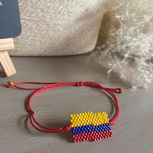 Op de afbeelding: Een rood koord armband met een gele, blauwe en rode kralen bedel in de vorm van de Colombiaanse vlag.