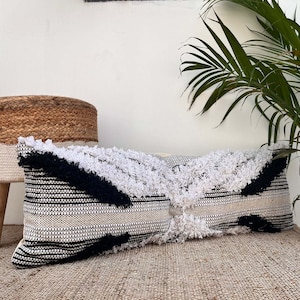 May include: A long, rectangular throw pillow with a black and white geometric pattern. The pillow has a fluffy, textured surface and is made of woven fabric.