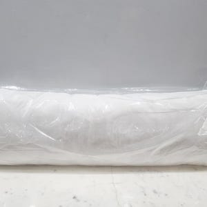 Puede incluir: Una almohada blanca rectangular y larga, envuelta en una bolsa de plástico transparente. La almohada está rellena de un material suave. El embalaje transparente permite ver la forma y el color de la almohada.