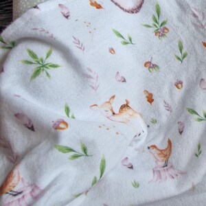 May include: White fabric with a repeating pattern of woodland animals, including deer, birds, and hedgehogs. The animals are illustrated in watercolor style with soft pink, brown, and green colors.
