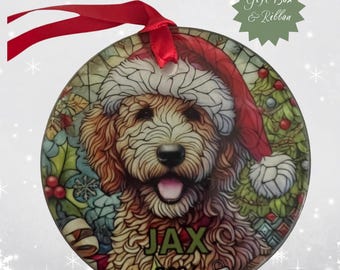 May include: Round Christmas ornament featuring a dog wearing a Santa hat. The dog's name, "JAX", and the year "2024" are printed on the ornament. A red ribbon is attached for hanging. The ornament has a stained-glass style design with a green gift box and ribbon.