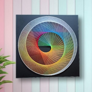 Puede incluir: Una pieza de arte con hilos de forma cuadrada que presenta un diseño circular creado con hilos vibrantes de múltiples colores dispuestos en un patrón en espiral sobre un fondo negro sólido, enmarcado en un borde negro fino.