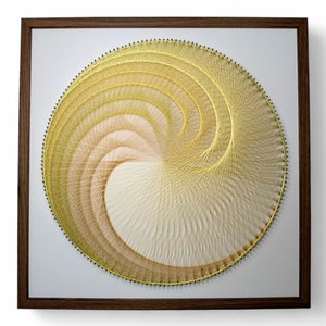 May include: A framed circular string art piece with a white background and a gold and beige spiral design.