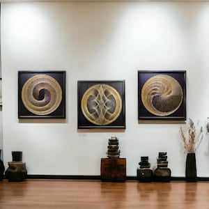May include: Three square framed wall art pieces featuring intricate gold string art designs on dark backgrounds. The two outer pieces display spiral patterns, while the center piece shows a symmetrical geometric motif. Below are dark wooden pedestals.