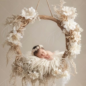 Peut inclure: Un nouveau-né dort dans un nid de fausse fourrure blanche, suspendu à un cerceau en bois décoré de fleurs blanches séchées et de verdure.