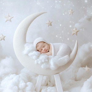 Könnte beinhalten: Ein neugeborenes Baby schläft friedlich auf einer weißen Halbmond-Requisite, umgeben von flauschigen weißen Wolken und funkelnden Sternen. Das Baby trägt eine weiße Strickmütze und ein Swaddle.