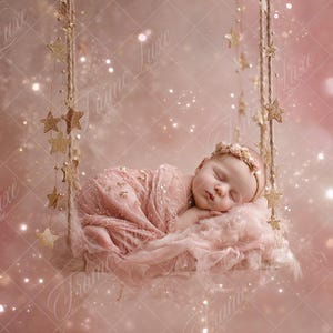 May include: A baby wrapped in pink fabric, asleep on a swing. The swing is adorned with gold stars and suspended by rope. The background is a soft pink with sparkling lights and a dreamy effect.