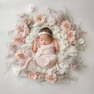 May include: A newborn baby wrapped in a light pink blanket, wearing a white headband, and sleeping peacefully. The baby is surrounded by a circular arrangement of soft, white and pink flowers and fluffy, light-colored fabric.