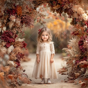 Könnte beinhalten: Ein junges Mädchen in einem weißen Kleid steht vor einem Blumenbogen. Der Bogen besteht aus getrockneten Blumen und Ästen, und das Mädchen lächelt. Der Hintergrund ist ein verschwommenes Bild von Herbstlaub.