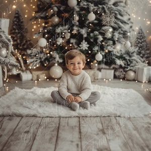 Può includere: Un bambino piccolo è seduto su un tappeto bianco e soffice davanti a un albero di Natale decorato. L'albero è decorato con palline bianche e argentate e luci. Il bambino indossa un maglione bianco e pantaloni grigi.