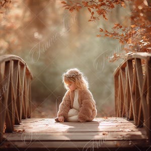 Puede incluir: Un niño pequeño con un abrigo marrón esponjoso y una corona de flores está sentado en un puente de madera. El puente tiene barandillas de madera y está rodeado de follaje otoñal. La escena está bañada en una luz cálida y suave.
