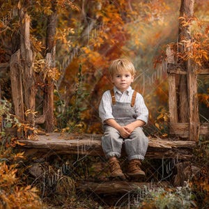May include: A young child sits on a rustic wooden bench, wearing overalls and boots. The scene is set outdoors with a weathered wooden fence and autumn foliage in shades of orange and brown.