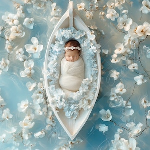 Pode incluir: Um bebê dormindo envolto em um cobertor branco e uma coroa de flores brancas está aninhado em um barco de madeira branco. O barco é cercado por flores brancas sobre um fundo azul claro.