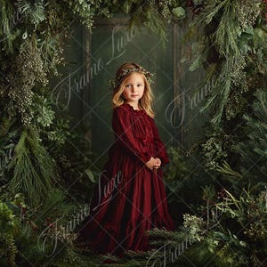 Puede incluir: Una niña con un vestido largo burdeos se encuentra entre una exuberante vegetación. Lleva una corona floral y está rodeada por un arco de ramas y follaje de hoja perenne. El fondo es de un verde oscuro apagado.