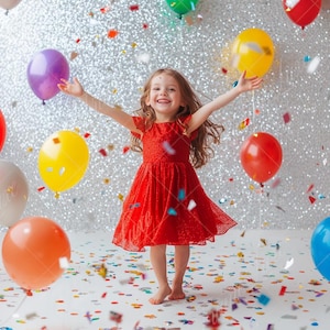 May include: A young girl in a red dress smiles and throws her arms up in the air as she stands in a room decorated with colourful balloons and confetti.
