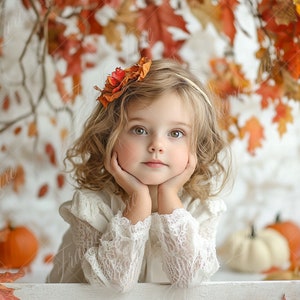 Może przedstawiać: Mała dziewczynka o kręconych blond włosach w białej koronkowej sukience i opasce z kwiatem siedzi z podbródkiem opartym na dłoniach. Jest otoczona jesiennymi liśćmi i dyniami.