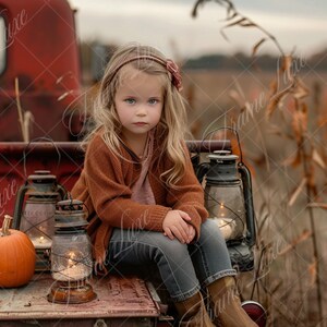 May include: A young girl with long blonde hair wearing a brown sweater and blue jeans sits on a red truck bed. She is holding a small pumpkin and there are three antique lanterns with lit candles on the truck bed.