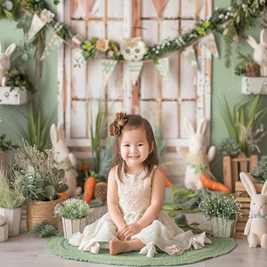 May include: A young girl wearing a white dress sits on a green rug in front of a rustic wooden door decorated with greenery and bunny decorations. She is surrounded by potted plants and faux bunnies.