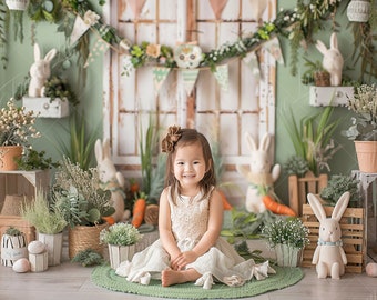 May include: A young girl wearing a white dress sits on a green rug in front of a rustic wooden door decorated with greenery and bunny decorations. She is surrounded by potted plants and faux bunnies.