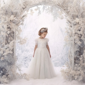 Könnte beinhalten: Ein junges Mädchen in einem weißen Spitzenkleid mit einer Blumenkrone steht in einer verschneiten Winterwunderland-Kulisse. Das Mädchen schaut nach unten und im Hintergrund ist ein verschneiter Wald mit einem weißen Torbogen zu sehen.