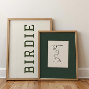 Puede incluir: Dos impresiones art&iacute;sticas enmarcadas. Una presenta la palabra "BIRDIE" en letras verdes sobre un fondo de cuadr&iacute;cula. La otra impresi&oacute;n tiene una ilustraci&oacute;n en blanco y negro de un golfista balanceando un palo, sobre un fondo verde oscuro.