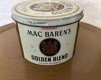 Op de afbeelding: Een witte blik met een rood en gouden etiket. Het etiket zegt "Reserved Mac Baren's Golden Blend Ready Rubbed" en heeft een wapenschild met een kroon en twee leeuwen. Gemaakt in Denemarken.