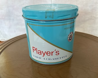 Op de afbeelding: Een blauwe metalen blik met de woorden "Player's Tabac à Cigarettes" en een gewichtsetiket met de tekst "Poids Net 20g".