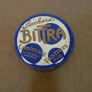 May include: A vintage round tin of Luchard BITTRA Chocolate Pastilles. The tin is blue and white with gold lettering. The text on the tin reads "BITTRA CHOCOLATE PASTILLES" and "BITTER SWEET CHOCOLATE". The net weight is 1/2 oz.