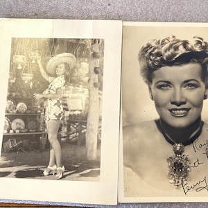 May include: Two vintage black and white photographs. One shows a woman in a floral romper and straw hat, posing outdoors. The other is a portrait of a woman with a necklace, signed "To May, with Best Wishes, Penny Singleton."