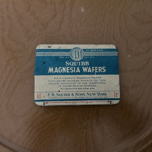 May include: A blue and white tin box with the text "SQUIBB MAGNESIA WAFERS" printed on it. The box is labeled "35 WAFERS" and has the text "Active Ingredient: Magnesium Hydrate" printed on it. The box is also labeled "E.R. SQUIBB & SONS, NEW YORK" and "MANUFACTURING CHEMISTS TO THE MEDICAL PROFESSION SINCE 1858".