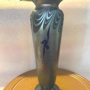 May include: An iridescent art glass vase with a flared top and a rounded base. The vase features a swirling pattern in shades of blue and silver, with a dark blue abstract design. The vase is approximately 10 inches tall.