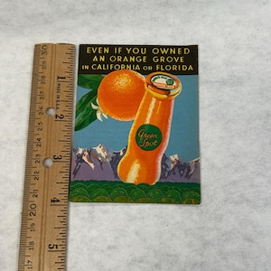 May include: Vintage advertisement for Green Spot Orange Ade. The image features an orange, a bottle of orange soda, and text that reads "Even if you owned an orange grove in California or Florida." A wooden ruler is on the left side.