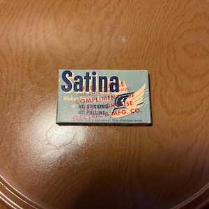 May include: A blue and white box with the text "Satina" in red letters. The box says "Makes Compliments" and "No Sticking, No Pulling" and "Electric Mfg. Co."