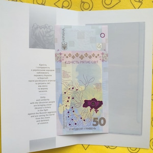 May include: A 50 hryvnia banknote from Ukraine with a purple and blue design. The banknote features a map of Ukraine with a tree-like pattern and the text "ЄДНІСТЬ РЯТУЄ СВІТ" (Unity Saves the World) in Ukrainian.