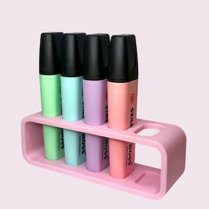 May include: A pink plastic holder with four highlighter pens. The pens are green, blue, purple, and pink. The pens have black caps and say "STABILO BOSS ORIGINAL" on the side.
