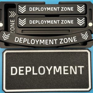 Może przedstawiać: Czarny organizer drukowany w 3D z białymi słowami "DEPLOYMENT ZONE". Organizer ma trzy sekcje z tekstem "DEPLOYMENT ZONE" i symbolami strzałek. Poniżej znajduje się prostokątny znak z napisem "DEPLOYMENT".
