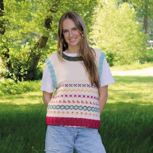 Op de afbeelding: Een mouwloos gebreid vest met een crèmekleurige basis en een veelkleurig fair isle-patroon in roze, geel en groen. Het kledingstuk heeft een donkergroene geribbelde halslijn, lichtblauwe geribbelde armsgaten en een felroze geribbelde zoom.