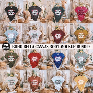 May include: A mockup bundle of 20 different colour t-shirts with the text "Your Design Here." printed on them. The t-shirts are displayed on hangers in a bohemian-style setting with wicker baskets and dried pampas grass.