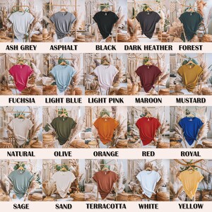 May include: A colour chart of 18 different t-shirt colours, including ash grey, asphalt, black, dark heather, forest, fuchsia, light blue, light pink, maroon, mustard, natural, olive, orange, red, royal, sage, sand, terracotta, white, and yellow.