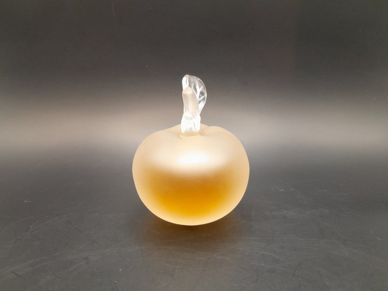 May include: A frosted glass perfume bottle shaped like an apple with a clear glass stopper. The bottle is filled with a light amber liquid.