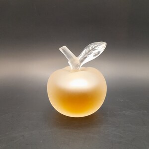 May include: A clear glass apple-shaped bottle with a frosted finish. The bottle has a clear glass stem and leaf.