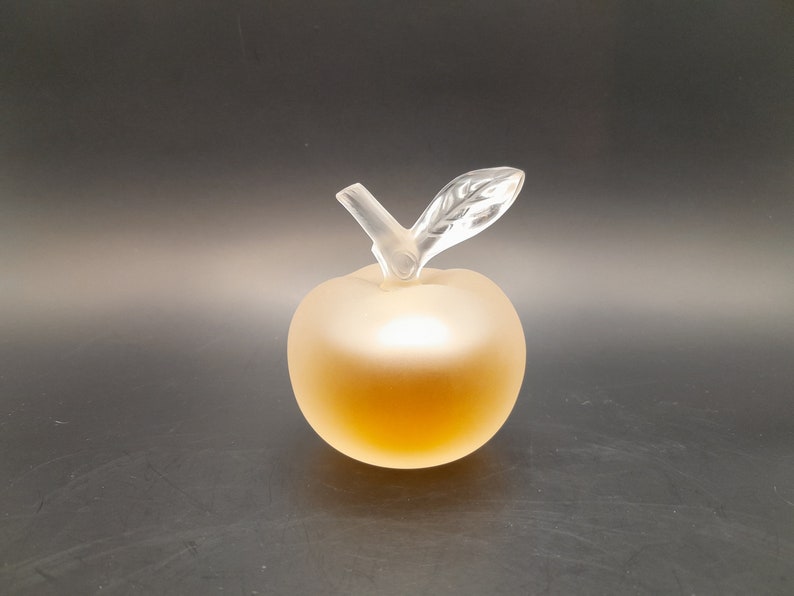 May include: A clear glass apple-shaped bottle with a frosted finish. The bottle has a clear glass stem and leaf.