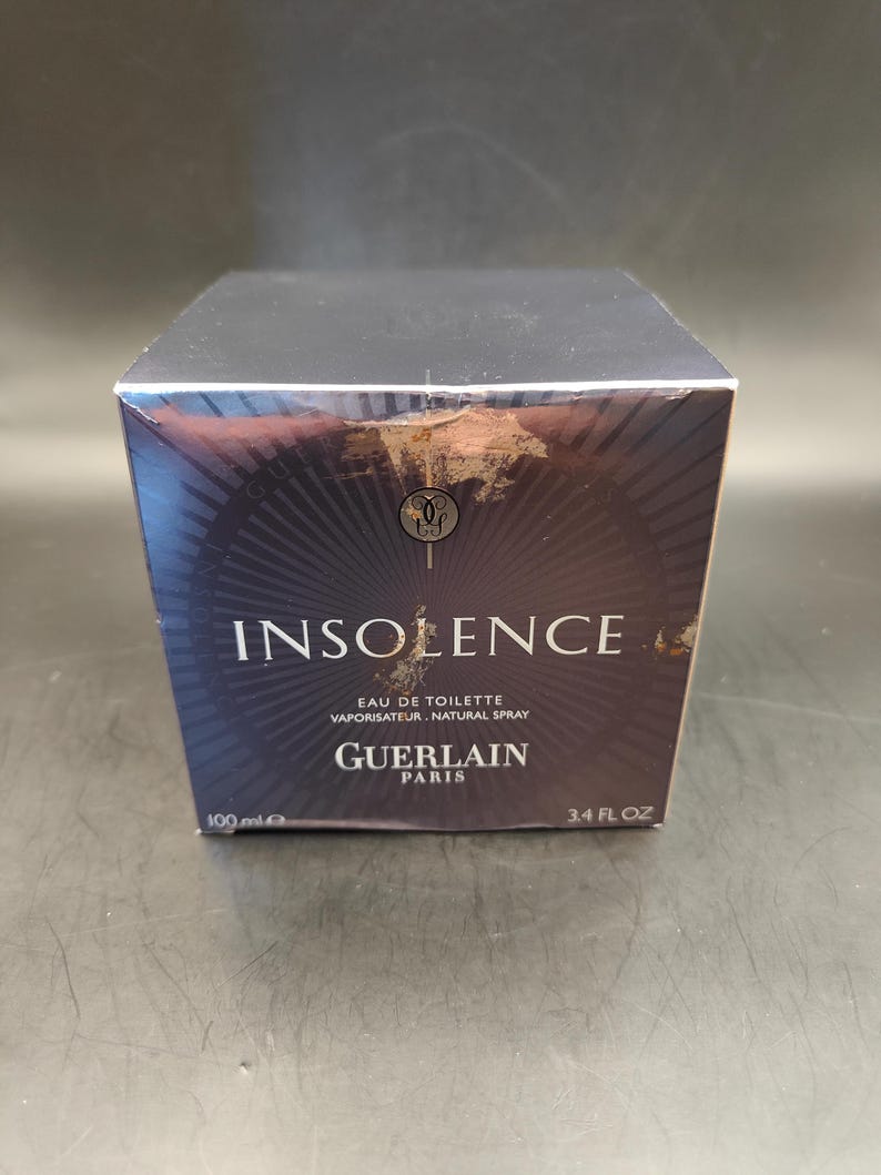 Puede incluir: Una caja negra con letras doradas para un frasco de 100 ml de Insoence Eau de Toilette de Guerlain Paris. La caja tiene un dise&ntilde;o negro y dorado con un patr&oacute;n de rayos de sol.
