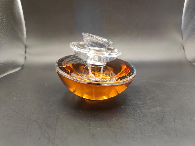 Puede incluir: Un frasco de perfume de vidrio transparente con una tapa de varios niveles. El frasco est&aacute; lleno de un l&iacute;quido &aacute;mbar dorado.