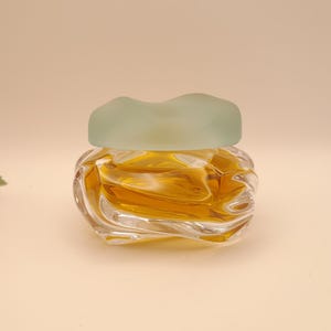 May include: A clear glass bottle with a textured design, filled with a golden liquid. The bottle has a frosted, light blue lid.