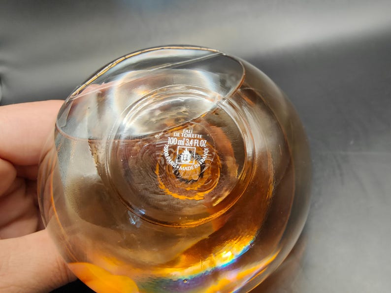 Puede incluir: Una botella de vidrio transparente con un l&iacute;quido dorado en su interior. La botella tiene una etiqueta que dice "Eau de Toilette 100 ml 3.4 fl oz" y "Made in France".