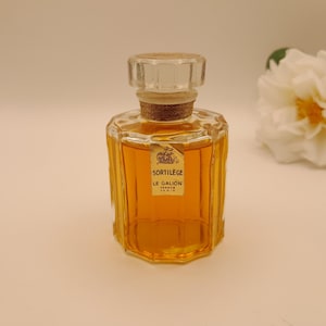 May include: A clear glass bottle of perfume with a gold cap and label. The label reads "Sortilege Le Galion France Paris".