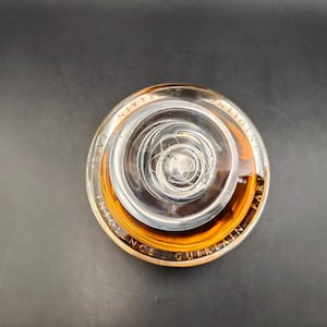 Puede incluir: Una botella de vidrio transparente con una tapa dorada y un l&iacute;quido marr&oacute;n en su interior. La botella est&aacute; etiquetada con "Insolence Guerlain Paris".