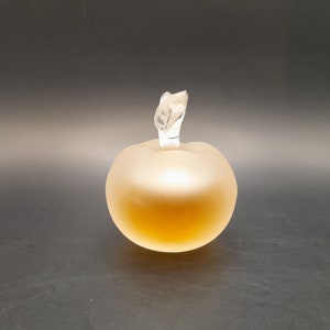 May include: A frosted glass perfume bottle shaped like an apple with a clear glass stopper. The bottle is filled with a light amber liquid.